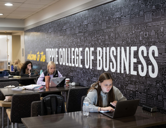 Students studying in a space with an accent wall displaying text that reads "Welcome to the Tippie College of Business."