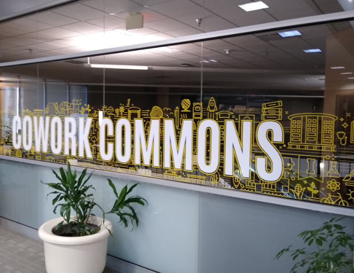 "Cowork Commons" displayed in large text over the brand community pattern on a window front