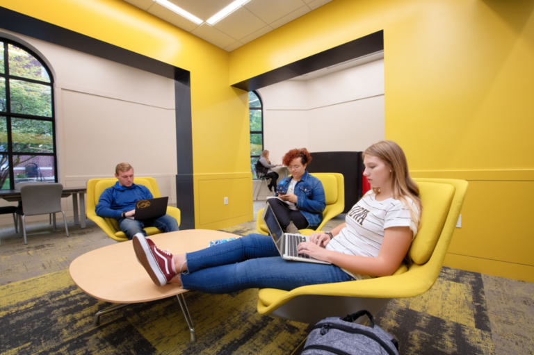 Students studying in Currier student lounge which has incorporated gold accent walls and furniture