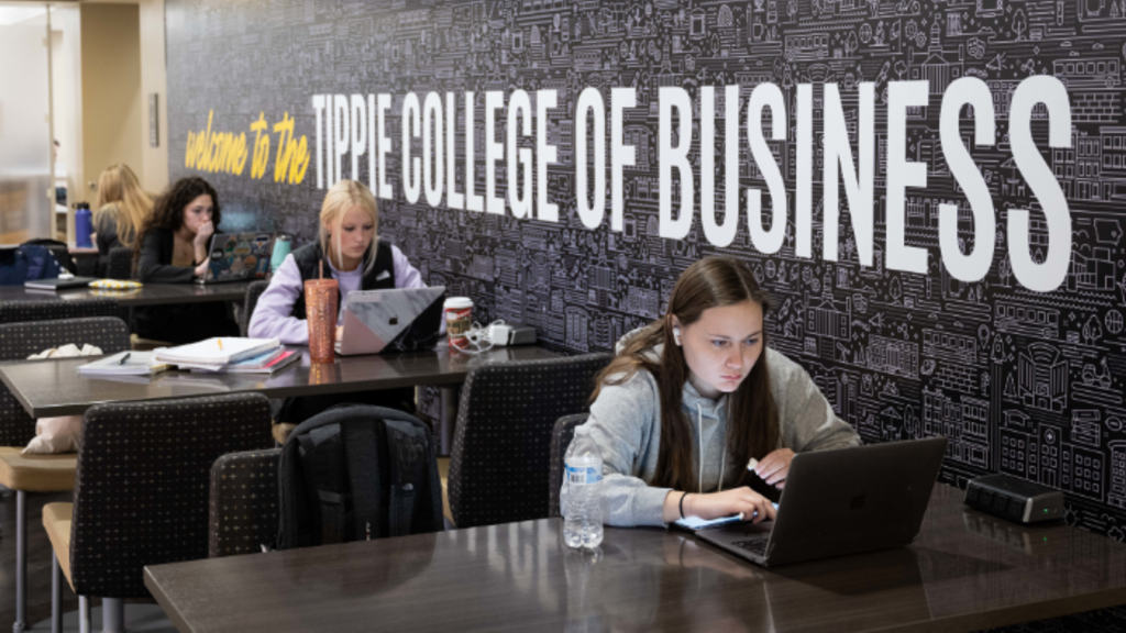 Students studying in a space with an accent wall displaying text that reads "Welcome to the Tippie College of Business."